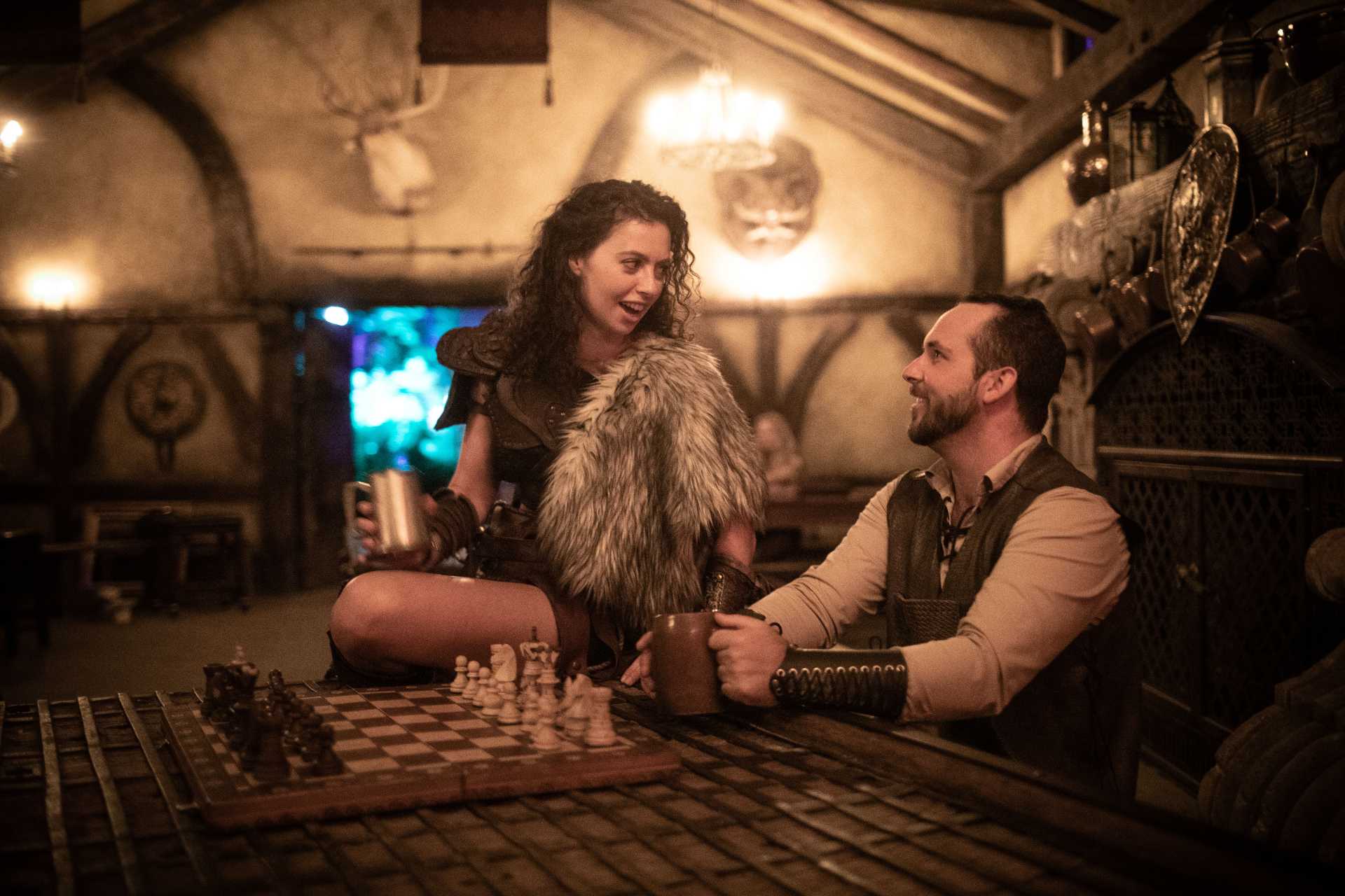 Two humans chat over drinks in a tavern in a dungeons and dragons world