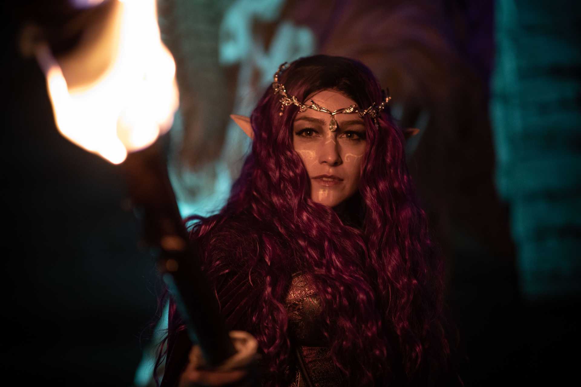 An elven woman holds a torch toward the camera