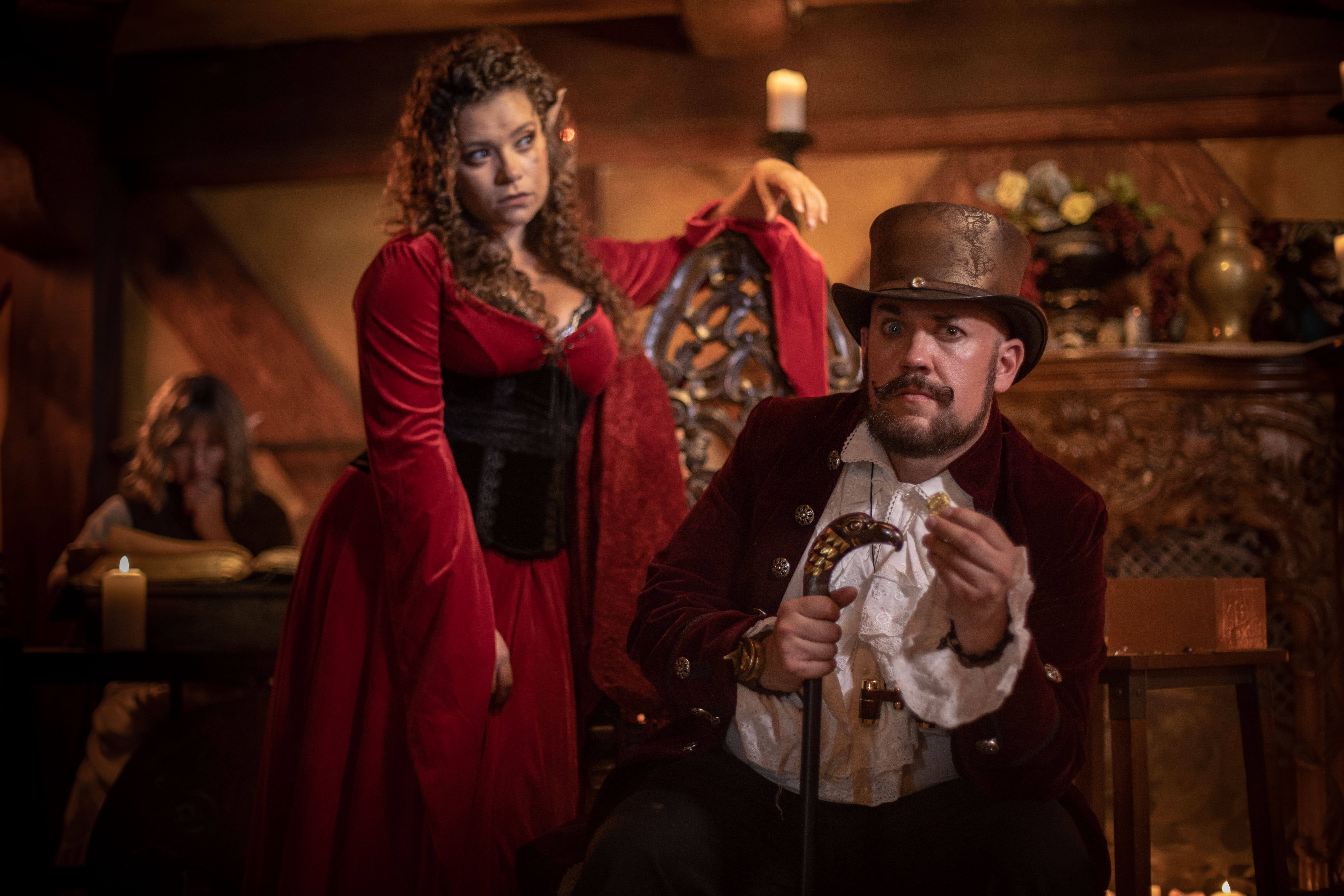 An elf in a red dress and a human in a top hat pose in a dungeons and dragons tavern